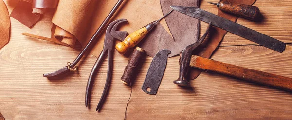 Leather craft tools on old wooden table. Leather craft workshop. Shoemaker\'s work desk. Tools and leather at cobbler workplace. Working tools on leather craftman\'s work desk.