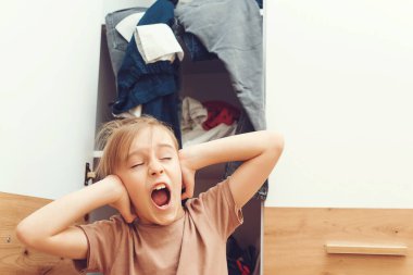 Stresli çocuk gardırobunu temizliyor. Gardırop ve soyunma odasında karışıklık. Giyecek bir şey yok. Genç çocuk dolapta kıyafet arıyor. Ev işleri..