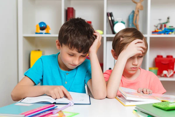 Home education, homeschooling. Tired kids are reading book at the table. Two schooler have stressed with difficult task and reading book. Boys are suffering from doing homework.