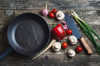 Ahşap arka planda mutfak aletleri ve baharatlar, üst manzara. Koyu ahşap masada yemek arkaplanı. Siyah tavayla yemek pişirmek için gerekli malzemeler. Yemek pişirmek için çeşitli ürünler.