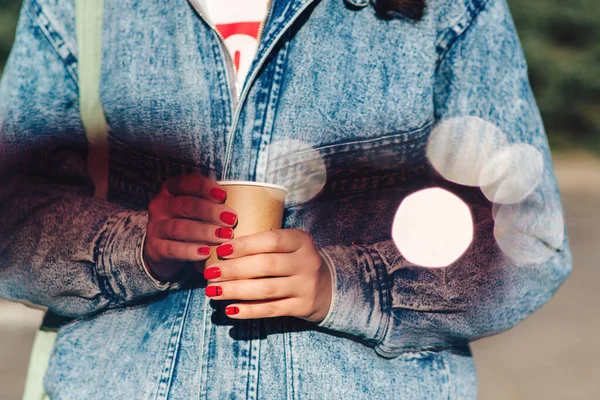 Hipster girl holding paper cup with coffee take away. Woman holding cup in hands. Drinking take away coffee. Paper coffee cup in woman hands with perfect manicure.