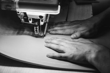 Deri işçiliğinin çalışma süreci. Tanner özel bir dikiş makinesine deri dikiyor, yakın çekim. İşçi dikiş makinesine deri ürün dikiyor. Deri işçisi atölyesi.