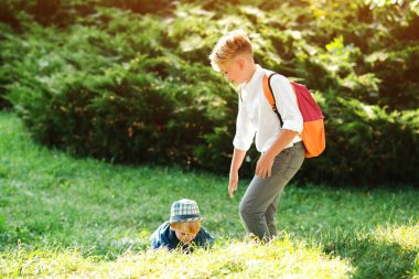 Çocuk küçük kardeşine yürüyüş yaparken elini uzatıyor. Okul çocuğu arkadaşını ekmesine yardım ediyor. Çocuklar birbirlerine yardım eder ve destek olurlar. Çocuklar yaz parkında birlikte yürüyorlar. Dışarıda mutlu kardeşler.