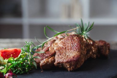 Siyah taş levhada ızgara biftek. Lezzetli ızgara biftek ve domatesli salata. Ana yemek sığır eti. Biftek ve salatalı akşam yemeği. Tahtada büyük para var..