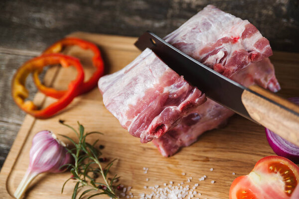 Butcher meat chopping knife and spices on wooden board. Top view of raw fresh pork ribs with spices. Raw fresh meat steak and meat cleaver on dark background. Butcher shop.