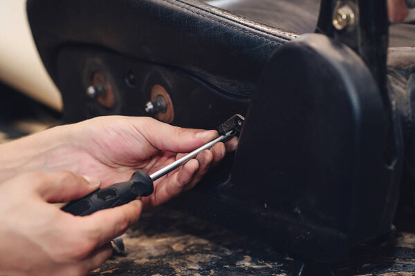 Repair of the old car seat. Car mechanic's hands is using tools. Working hands of a man at the car service, close up.