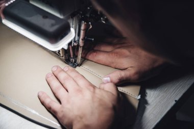 Deri işçiliğinin çalışma süreci. Tanner özel bir dikiş makinesine deri dikiyor, yakın çekim. İşçi dikiş makinesine deri ürün dikiyor. Deri işçisi atölyesi.