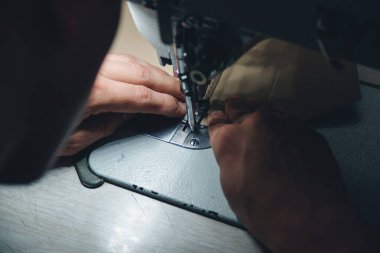 Deri işçiliğinin çalışma süreci. Tanner özel bir dikiş makinesine deri dikiyor, yakın çekim. İşçi dikiş makinesine deri ürün dikiyor. Deri işçisi atölyesi.