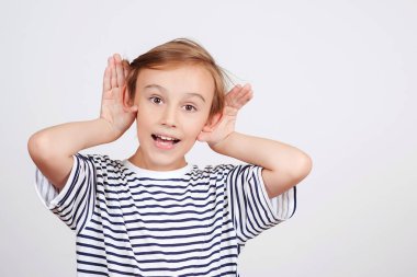 Komik çocuk portresi bir şeyler dinliyor. Tatlı çocuk kulağının dibinde el ele tutuşuyor. Çocukla aile iletişimi. Ebeveynleri dinleyin. Beyaz geçmişi olan bir okul çocuğu. Okulda çocukların dedikodu duyması. Yüz ifadesi