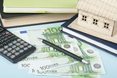 Ev tasarruf, bütçe kavramı. Model ev, not defteri, kalem, hesap makinesi ve sikkeler üzerinde ahşap ofis Resepsiyon Masası.