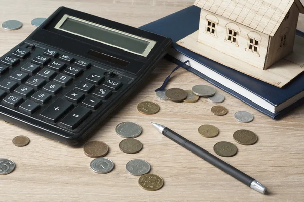 Ahorro en el hogar, concepto de presupuesto. Casa modelo, bloc de notas, pluma, calculadora y monedas en mesa de escritorio de oficina de madera . — Foto de Stock