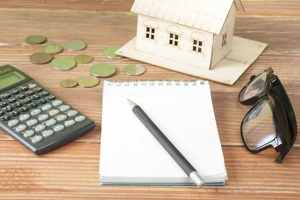Ahorro en el hogar, concepto de presupuesto. Casa modelo, bloc de notas, pluma, calculadora y monedas en mesa de escritorio de oficina de madera . — Foto de Stock