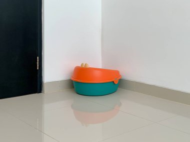 Canlı bir turuncu ve deniz mavisi eğitim koltuğu beyaz duvarları ve kullanıma hazır koyu renkli kapısı olan bir odanın köşesine yerleştirilir..