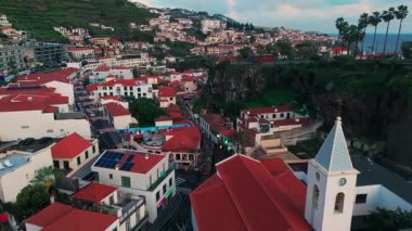 Gökyüzü kıyı köyü kırmızı çatı evleri, alacakaranlık ışığı ve dar kaldırımlı caddelerin üzerindeki kilise kulesi kayalık uçurumlar içine düşüyor. Camara de Lobos, Madeira, Portekiz