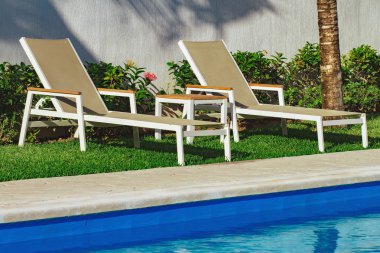 Havuzun yanında iki şezlong. Yaz aylarında şezlonglu modern yüzme havuzu. Rahatlatıcı havuz yüzme iki şezlong. Havuz açık. Bahçeden görünüm.