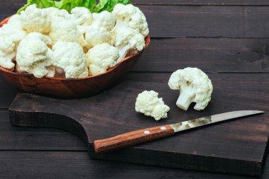 Masada karnabahar var. Karnabahar ahşap kase kahverengi masada yatıyor. Keskin paslanmaz bıçaklı kesme tahtası.