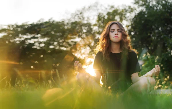 A menina medita na grama ao pôr do sol — Fotografia de Stock