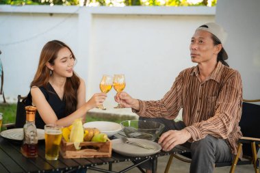 A group of multiracial friends are having a backyard dinner party, clinking beers or sharing drinks during happy hour. Young people are having fun together and clinking beers while standing in the garden.