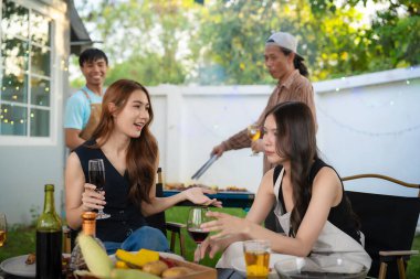 A group of multiracial friends are having a backyard dinner party, clinking beers or sharing drinks during happy hour. Young people are having fun together and clinking beers while standing in the garden.