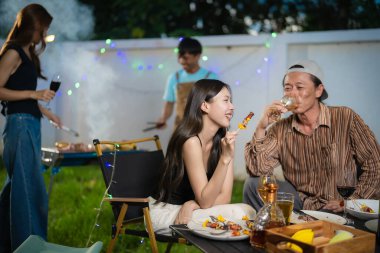 A group of multiracial friends are having a backyard dinner party, clinking beers or sharing drinks during happy hour. Young people are having fun together and clinking beers while standing in the garden.