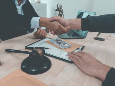 Law Firm, Agreements and Partnerships Two professionals in suits shake hands, a gavel strikes documents and the scales of justice lie on the table in front of them.