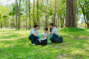 Gönüllüler parkta çöp toplar, bölgeyi temizler, gönüllü konsept, hayır kurumu, insanlar ve ekoloji, Asyalı aile plastik atık toplar, Dünya Temizlik Günü