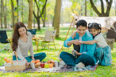 Mutlu Asyalı aile yaz tatilinde parkta piknik yapıyor. Çocuk anne ve babasıyla birlikte parkta gezinin tadını çıkarıyor. Güzel doğa..
