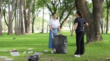 İki Asyalı kadın parkta çöp torbalarıyla plastik şişe topluyor ve park alanını temizlemenin keyfini çıkarıyorlar..