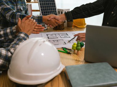 Anlaşma tamamlandıktan sonra mühendis ve mimarın el sıkışması, güvenlik yelekleri giyen inşaat işçileri, inşaat alanında takım çalışması.