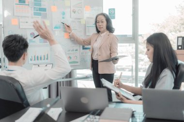 Bir grup iş adamı çalışma masalarında birlikte çalışan ve belgeleri tartışan çalışma arkadaşlarının sonuçlarını gösteren çizelge ve grafikleri tartışıyor..