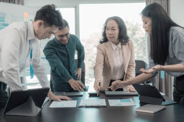 Bir grup iş adamı çalışma masalarında birlikte çalışan ve belgeleri tartışan çalışma arkadaşlarının sonuçlarını gösteren çizelge ve grafikleri tartışıyor..