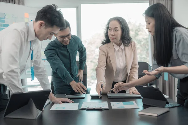 Bir grup iş adamı çalışma masalarında birlikte çalışan ve belgeleri tartışan çalışma arkadaşlarının sonuçlarını gösteren çizelge ve grafikleri tartışıyor..