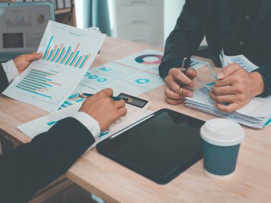 İş adamları takım çalışmasının sonuçlarını, etkin veri analizini ve maliye bakanlığının planlamasının başarısını gösteren çizelge ve grafikleri tartışıyor..