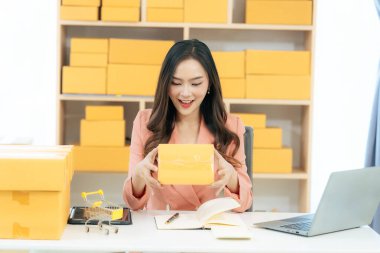 Asian woman using laptop with box, successful cheerful for online marketing packaging and delivery concept SME, small business entrepreneur, SME freelancer.