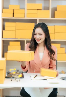 Asian woman using laptop with box, successful cheerful for online marketing packaging and delivery concept SME, small business entrepreneur, SME freelancer.