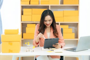 Asian woman using laptop with box, successful cheerful for online marketing packaging and delivery concept SME, small business entrepreneur, SME freelancer.
