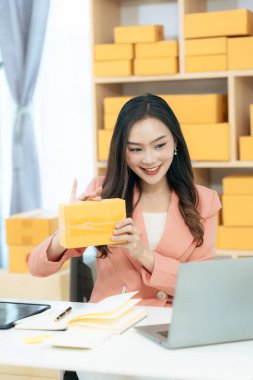 Asian woman using laptop with box, successful cheerful for online marketing packaging and delivery concept SME, small business entrepreneur, SME freelancer.