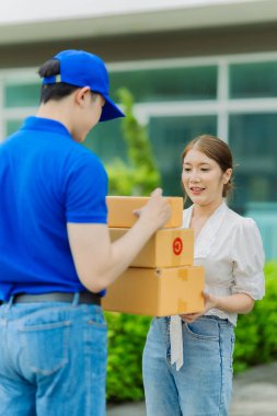 Mavi gömlekli teslimatçı, ön kapıdaki genç bayan müşteriye paketlenmiş malları teslim ediyor.