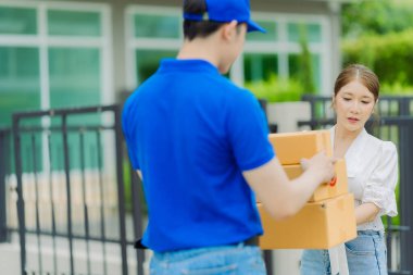 Mavi gömlekli teslimatçı, ön kapıdaki genç bayan müşteriye paketlenmiş malları teslim ediyor.