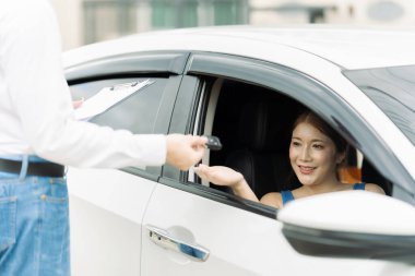 Genç Asyalı bir adam yeni bir araba aldıktan sonra araba anahtarlarını genç bir kadına verir. Satın alma, satma, kiralama, araba anahtarlarını teslim etme, araba satış sözleşmesi, iş anlaşması.
