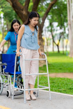 Kadın bir doktor, yaşlı bir Asyalı kadına yeşil doğada cesaret ve rahatlık vererek bastonla yürümeyi öğrenmesine yardım eder..