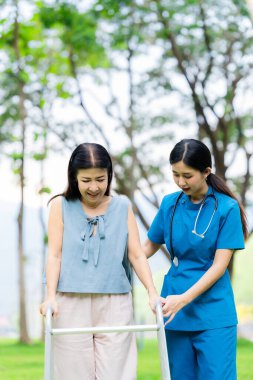 Asyalı hemşire ve yaşlı kadın hasta parkta el ele tutuşuyorlar. Emeklilikte yaşlılara bakım kavramı. Sağlık Hizmetleri Merkezi.