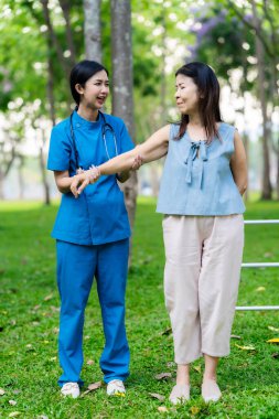 Asyalı hemşire ve yaşlı kadın hasta parkta el ele tutuşuyorlar. Emeklilikte yaşlılara bakım kavramı. Sağlık Hizmetleri Merkezi.