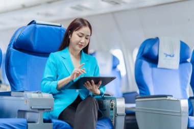 Uçakla seyahat ederken dijital tablet kullanan Asyalı kadın. Pencerenin yanındaki kabinde dijital cihaz kullanan bir kadın yolcu. İş seyahatinde..