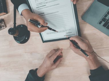 Ofisinde çalışan bir erkek avukat, ofisinde oturan tokmak ve terazili bir erkek müvekkil ile sözleşme imzalıyor. (Yakın çekim)