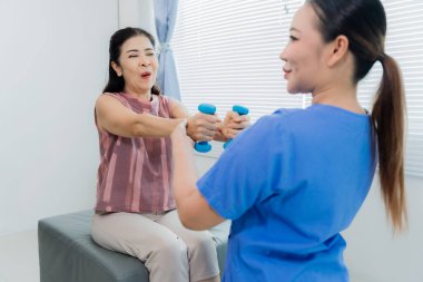 Asyalı bir kadın fizyoterapist yaşlı bir hastaya kas rehabilitasyonuna yardım etmek için fizik tedavi uyguluyor..