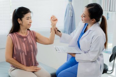 Asyalı bir kadın fizyoterapist yaşlı bir hastaya kas rehabilitasyonuna yardım etmek için fizik tedavi uyguluyor..