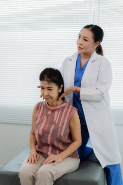 Asyalı bir kadın fizyoterapist yaşlı bir hastaya kas rehabilitasyonuna yardım etmek için fizik tedavi uyguluyor..