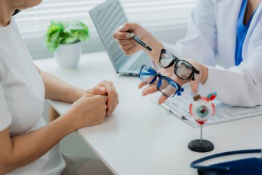 Bir doktor ve bir hasta bir masada oturmuş miyopluk, sağlık ve ilaç kavramlarının tedavisini tartışıyorlar..