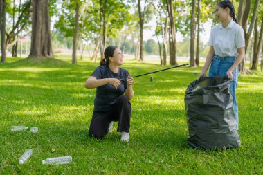İki Asyalı kadın parktaki çimlerden çöp topluyor. Gündüz vakti çevre temizliğine katılıyorlar..